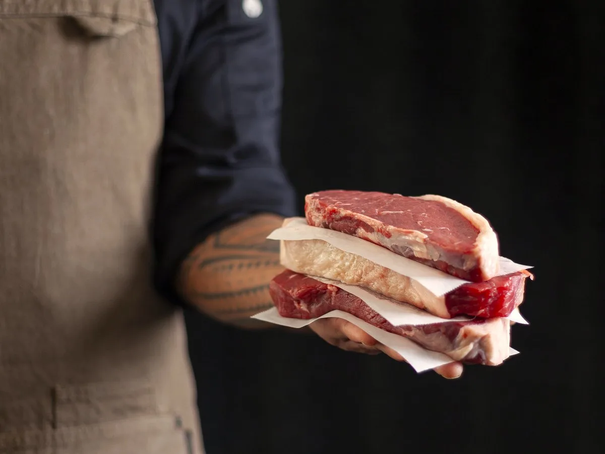 The butcher handing steaks across the counter.
