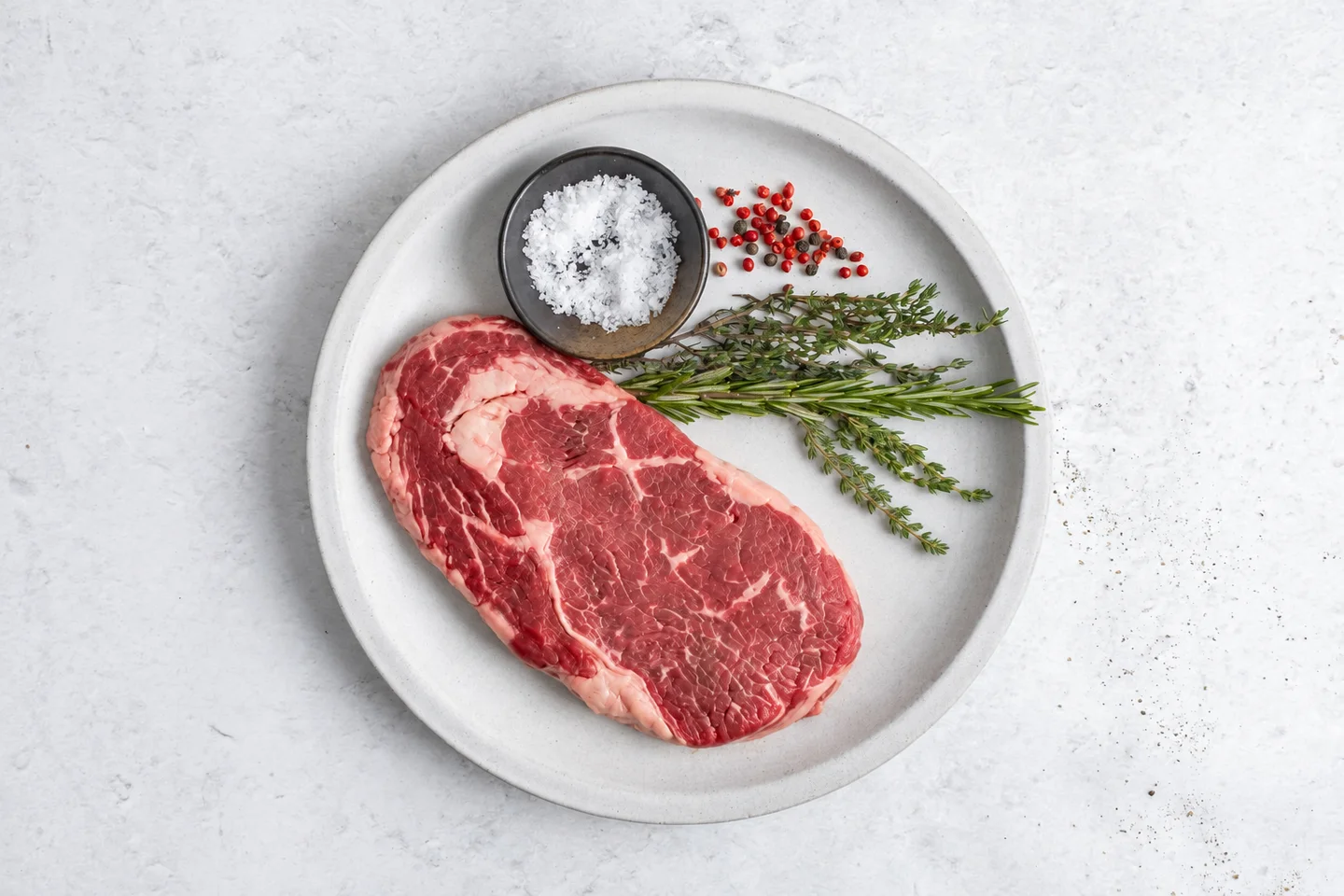 Raw ribeye on a ceramic plate with herbs and salt