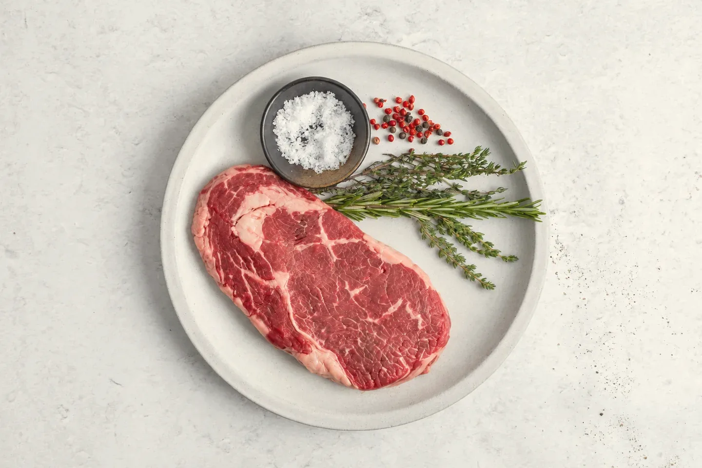 Raw ribeye on a ceramic plate with herbs and salt